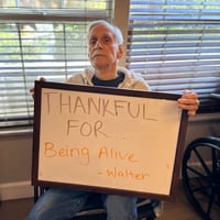 a resident of pacifica senior living Bakersfield holds a board saying he is thankful to be alive
