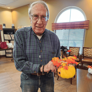 a resident of pacifica senior living holds up a a pumpkin he painted craft