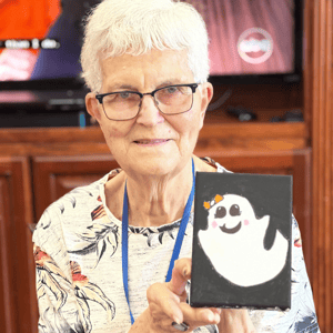 pacifica senior living resident holds up her painting of a ghost for halloween