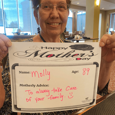 pacifica senior living resident hols a sign showing mothers day advice