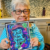 a senior woman resident of pacifica senior living mission villa holds up her coloring book art that says just be you