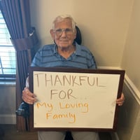 a resident of pacifica senior living Bakersfield holds a board saying he is thankful for a loving family