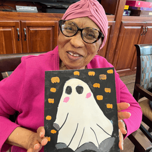 a resident of pacifica senior living holds up a painting of a spooky ghost she made