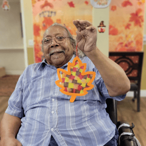 a resident of pacifica senior living holds up a crafted stained glass leaf made from colored paper