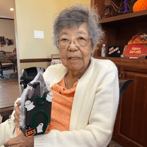 a resident of pacifica senior living holds up a paper crafted haunted house she made