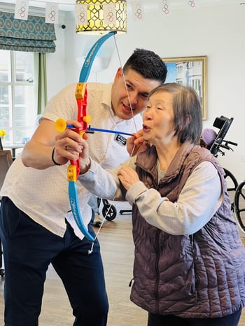 George the activities director of mission villa shows a resident how to use a plastic bow and arrow