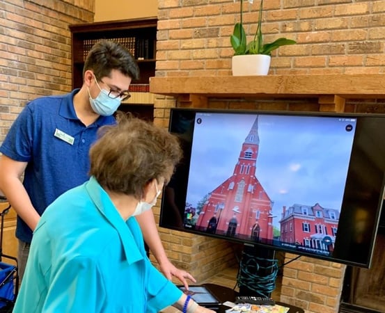 a caregiver shows a resident how to use tech in a pacifica senior living community