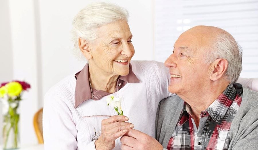 a senior couple smiling and holding a flower