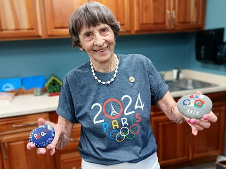 A pacifica senior living resident shows off her painted olympic rock craft