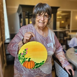 a resident of west park senior living shows off her painted circle door hanger with pumpkins and fall decor